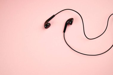 Pembe pastel arka planda izole edilmiş siyah kulaklık. Düz yat. Uzay boşluğu. müzik minimalizmi