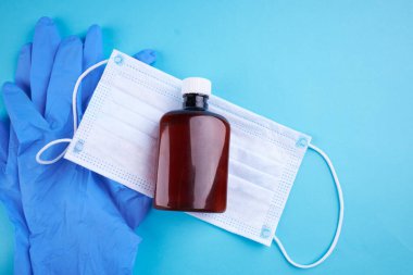 Sabun şişesi mavi arka planda beyaz tıbbi maskenin üzerinde duruyordu. düz yat