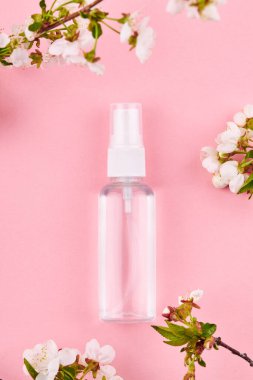 İçinde şeffaf sıvı olan bir şişe. Alkol el dezenfektanı çiçek desenli pembe arkaplan üzerine
