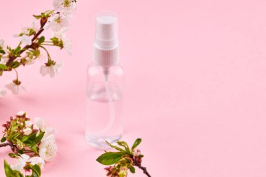 İçinde şeffaf sıvı olan bir şişe. Alkol el dezenfektanı çiçek desenli pembe arkaplan üzerine