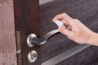 Alkol spreyi dezenfekte ederek kapı kolunu dezenfekte eden kişi.