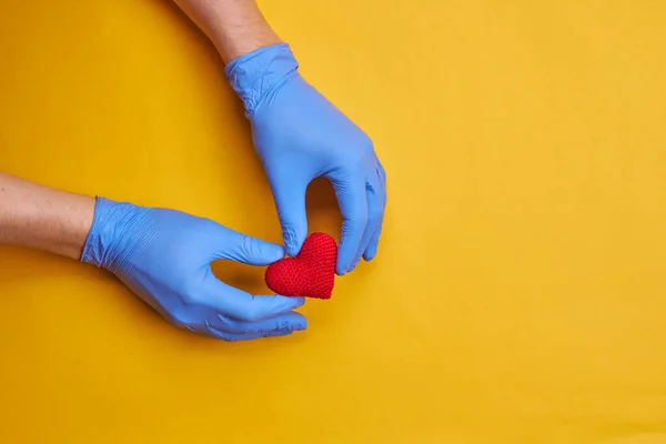 Símbolo rojo del corazón a la mano de las personas con guantes médicos azules. fondo amarillo o naranja con espacio de copia. concepto de enfermedad cardíaca — Foto de Stock