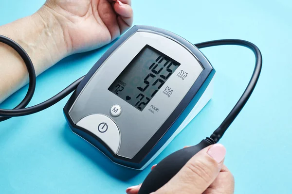 Měření krevního tlaku s elektronickým zdravotnickým zařízením přes modré pozadí — Stock fotografie
