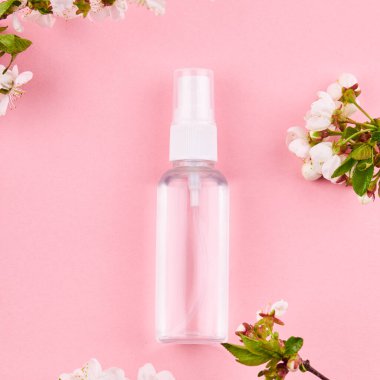 İçinde şeffaf sıvı olan bir şişe. Alkol el dezenfektanı çiçek desenli pembe arkaplan üzerine