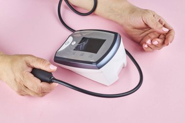 Pembe arka planda elektronik tıbbi cihazla kan basıncı ölçülüyor.