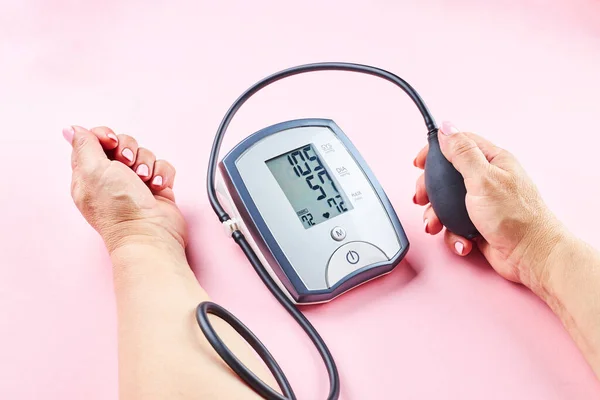 Měření krevního tlaku s elektronickým zdravotnickým zařízením přes růžové pozadí — Stock fotografie