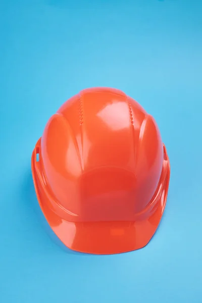 orange protective helmet and safety glasses near it on a bright blue background. protective workwear and construction industry concept