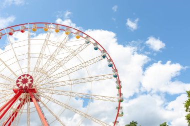 Lunaparktaki devasa dönme dolap. Mavi gökyüzünde. Arka planda bulutlar var. Şenlik ve eğlence havası.