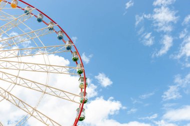 Lunaparktaki devasa dönme dolap. Mavi gökyüzünde. Arka planda bulutlar var. Şenlik ve eğlence havası.