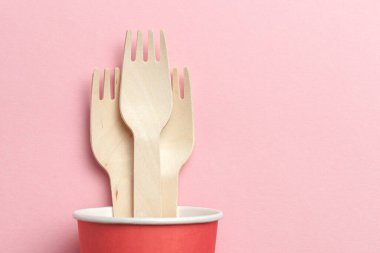 Çevre dostu ve tek kullanımlık mutfak eşyaları. Kağıt bardaktaki ahşap çatallar pembe mercan arka planda. Düz yat. Boşluğu kopyala