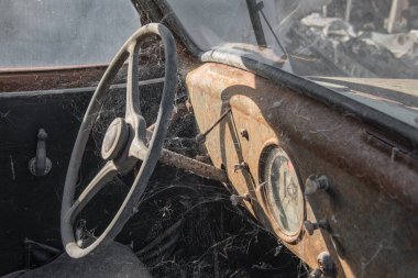 Eski paslı bir arabanın yakın plan görüntüsü. Sol elle çekiş ve direksiyonu ve paslı ve örümcek ağlarıyla kaplı konsolu gösteriyor.