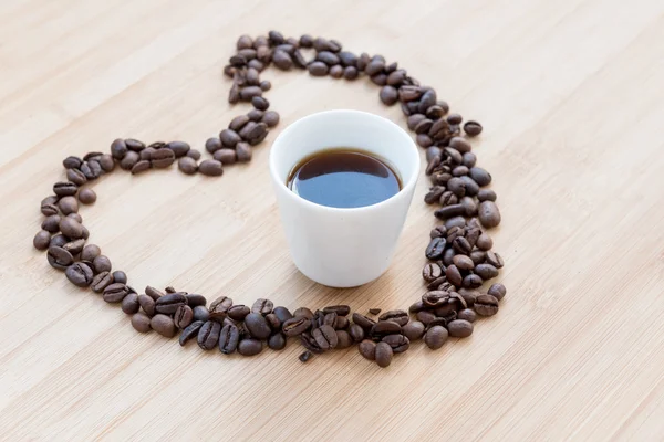 Grãos de café e xícara preta de café dentro de um coração — Fotografia de Stock