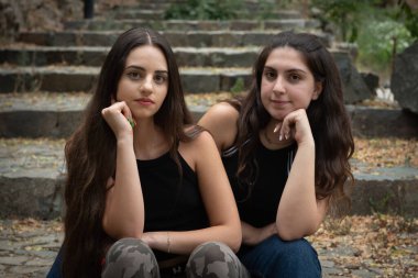 Taş gibi bir merdivende oturup kameraya bakan iki güzel ve çekici genç kadının portresi..