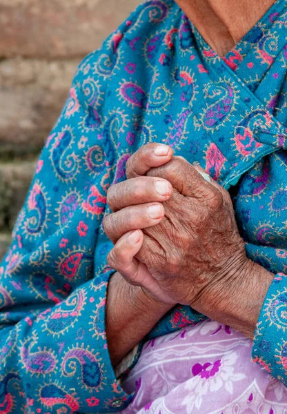Nierozpoznana starsza kobieta ubrana w niebieskie szmaty krzyżujące jej pomarszczone ręce. Proces starzenia się społeczeństwa — Zdjęcie stockowe