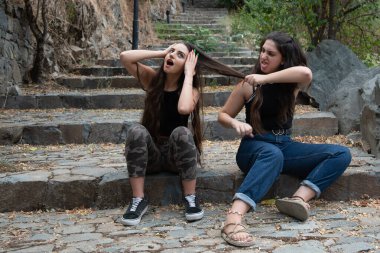 İki kadın kavga ediyor ve taşlı bir merdivende otururken saçlarını çekiştiriyorlar. Arkadaşlık eşleşmesi.