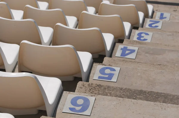 Weiße Plastik leere Stadion- oder Bühnenstühle in einer Reihe und nummerierte Stufen. Stockbild