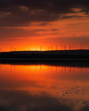 Gölde gün batımı ve tepenin yamacında alternatif enerji için rüzgar türbinleri..