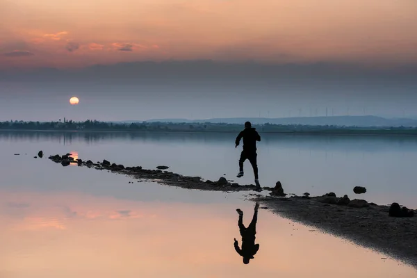 인지되지 않은 사람이 태양을 향해 달려가고 있습니다. 목가적 인 겨울 일몰, 호수에서. — 스톡 사진