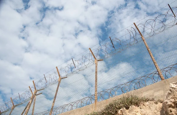 Security fence with barbed wire against a blue cloudy sky — Stock Photo, Image