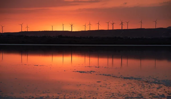 日落在湖畔，风力涡轮机在山坡上寻找替代能源. — 图库照片