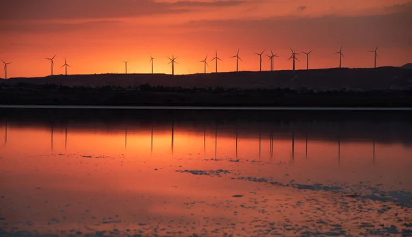 Pôr do sol no lago e turbinas eólicas para energia alternativa na encosta da colina. — Fotografia de Stock