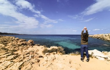 Bilinmeyen bir kadın kayalık bir sahilde mavi denizin tadını çıkarıyor.
