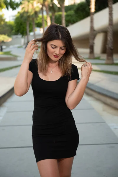 Young attractive shy woman wearing black stylish dress looking down walking in the street — Stock Photo, Image