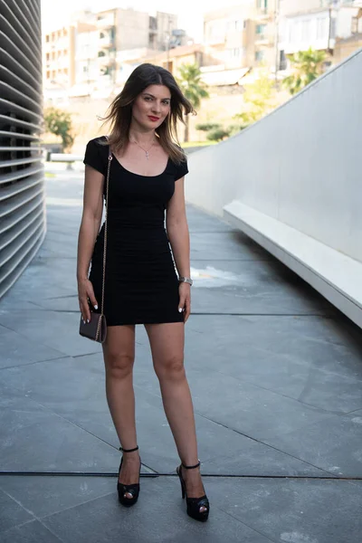 Молодая привлекательная девушка в черном стильном платье и маленькой рубашке позирует на улице — стоковое фото