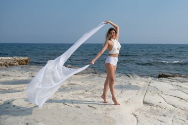 Okyanusun kıyısındaki kayalık bir sahilde dans eden genç bir kadın.