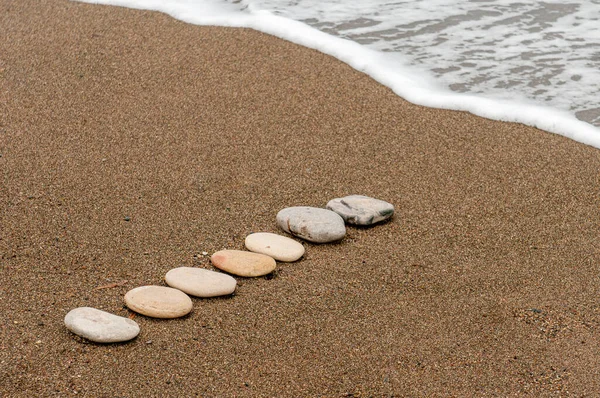 Piedras de playa lisas en un crudo en una costa arenosa y espuma de agua de mar. — Foto de Stock
