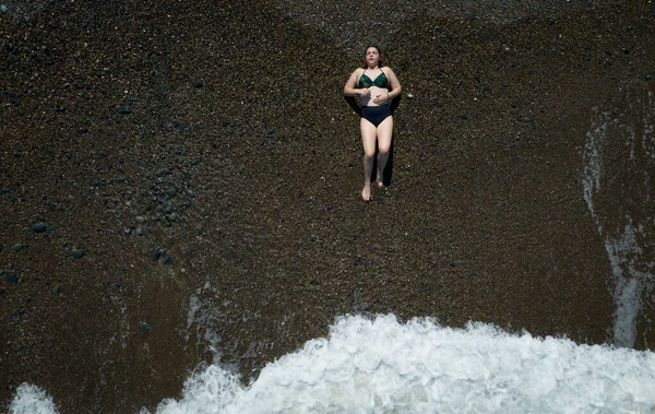 Mayosu olan bir kadın kumlu bir sahilde dinleniyor ve kıyıda fren dalgaları var. Tepeden. Hava aracı fotoğrafı. — Stok fotoğraf