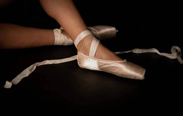 Pernas de bailarina jovem que coloca em sapatos pontiagudos no fundo do chão preto. Prática de balé. — Fotografia de Stock