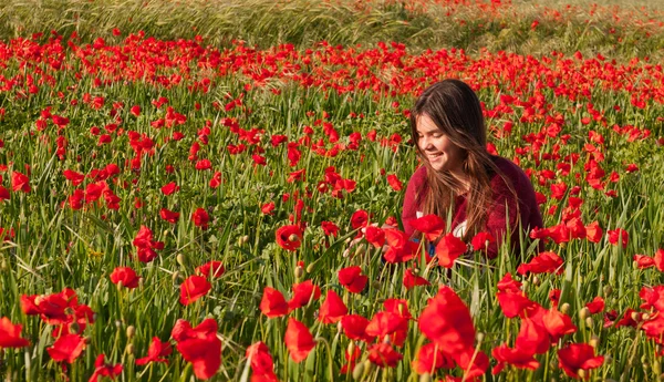 Feliz adolescente sonriente sentada en un campo de amapola roja Imagen de stock