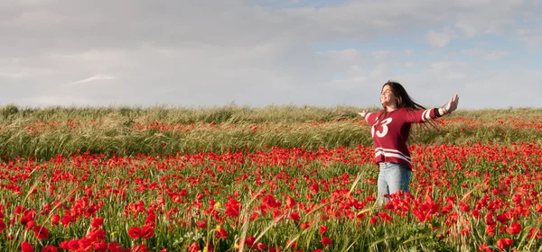 Mutlu genç kız ayakta haşhaş çiçek kırmızı bir alan içinde — Stok fotoğraf