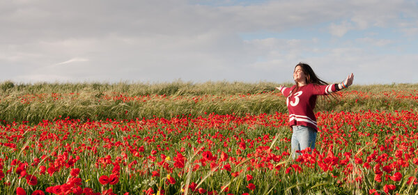 Happy Teenage Girl standing  in a red field of poppy flowers 