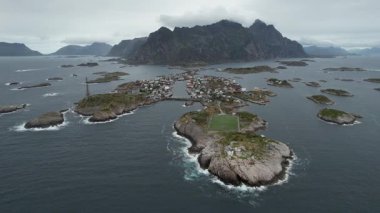 Henningsvaer 'in 4k insansız hava aracı, Norveç' in Lofoten şehrinde pitoresk bir balıkçı köyü. Güneşin doğuşunda bir futbol sahası ve kayalık bir sahil manzarası.