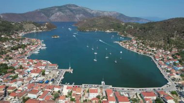 Dağlar ve yemyeşil yeşilliklerle çevrili bir Yunan adası olan Ithaki 'deki Serene limanının insansız hava aracı görüntüleri. Yelkenliler berrak mavi sularda, parlak bir gökyüzünün altında huzur içinde yüzerler..