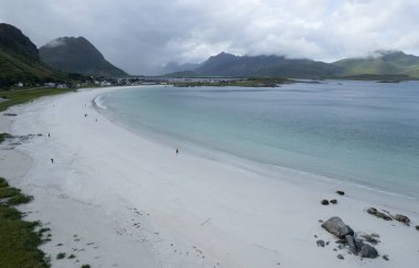 Ramberg plajının keyfini çıkaran turistlerin insansız hava görüntüsü. Rambergstranda, Lofoten Adaları, Norveç 'te bulutlu bir yaz gününde.