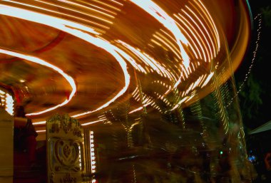 Dönen bir atlıkarıncanın parlak çizgileri, panayırdaki bir gecenin enerjisini ve heyecanını yakalıyor.