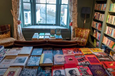 Whitstable, Birleşik Krallık, 21 Kasım 2025: Pencere manzaralı sıcak, davetkar bir edebiyat dükkanının içindeki rafları ve masaları dolduran kitaplar