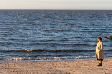 Trençkotlu bir kadın gün batımında kumsalda durmuş denize bakıyor. Whitstable Kent Birleşik Krallık