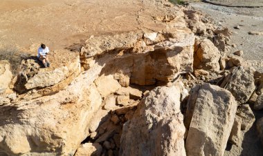 Kuru çöl manzarasında aşınmaya bakan kaya oluşumunda oturan kadın.