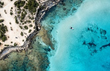 Görünür kayalıkları olan kayalık bir sahil şeridinin yanında, turkuaz bir okyanus suyuna bağlı İHA antresi. Mavi Göl Akamas Yarımadası Kıbrıs