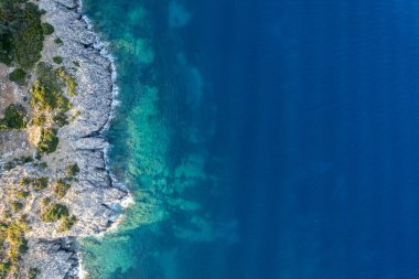 Turkuaz deniz suyunun hava aracı görüntüsü güneşli bir yaz gününde kayalık bir sahil şeridiyle buluşuyor.