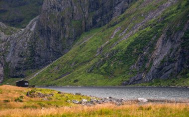 Dik, yeşil yamaçlı ve kayalık arazili dağ gölü kıyısında ücra bir kulübe. Eggum Lofoten Adaları, Norveç