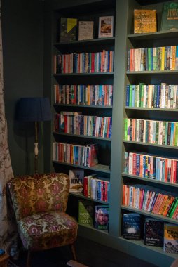 Whitstable, Birleşik Krallık, 21 Kasım 2025: Bir kitapçıda kitaplarla dolu olan rahat okuma köşesi, şablon, yer lambası ve duvara monte edilmiş kitaplıklar