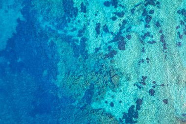 Titreyen turkuaz su mercan oluşumlarını ve yukarıdan gelen kaya yatağını ortaya çıkarıyor.