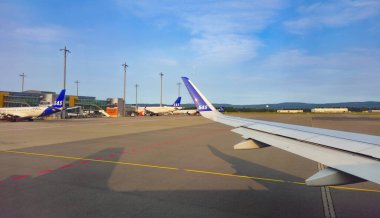 Oslo, Norveç, 9 Ağustos 2025: Pencereden görünen uçak kanadı, terminale birden fazla sas uçağı yanaştı