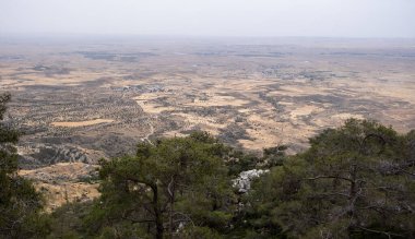 Bir dağın tepesinden çarpıcı bir manzara geniş kurak alanlar ve uzaktaki dağınık köyleri ortaya çıkarıyor. Sahne bulutlu bir gökyüzü altında manzaranın doğal güzelliğini ve huzurunu yakalar. Lefkoşe Bölgesi Kıbrıs