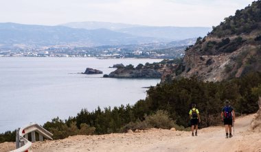 Akdeniz manzaralı bir toprak yolda yürüyen iki kişi ve Akamas yarımadasındaki uzak bir tatil köyü, Cythe.